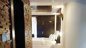 A modern bedroom with a brick accent wall, a bed with white linens, and a nightstand with a lamp. - Pearl Park Beach Resort Private Limited (Port Blair)