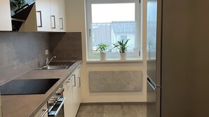 A modern kitchen with a built-in oven, a stainless steel refrigerator, and a window with potted plants.