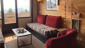 Una habitación acogedora con un sofá, un sillón rojo, una mesa de centro y un ventanal con vistas a las montañas.