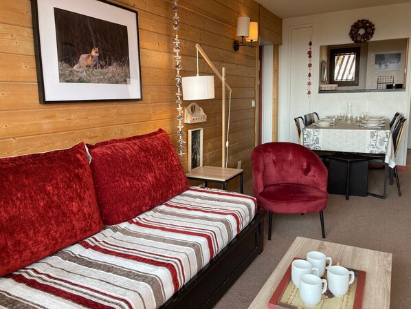 A cozy living room with a red sofa, a dining area with a table set for four, and a framed picture on the wall. - Apartment for 6/7 pers, mountain view, small pets welcome (Avoriaz)