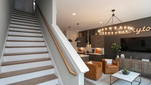 Ein zeitgemäßer Wohnraum mit Treppe, Küchenbereich, Sitzecke mit Couchtisch und großem Fernseher.