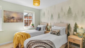Ein Schlafzimmer mit zwei Betten, einem Fenster, einem Bild und einer Wandmalerei mit Waldmotiv.
