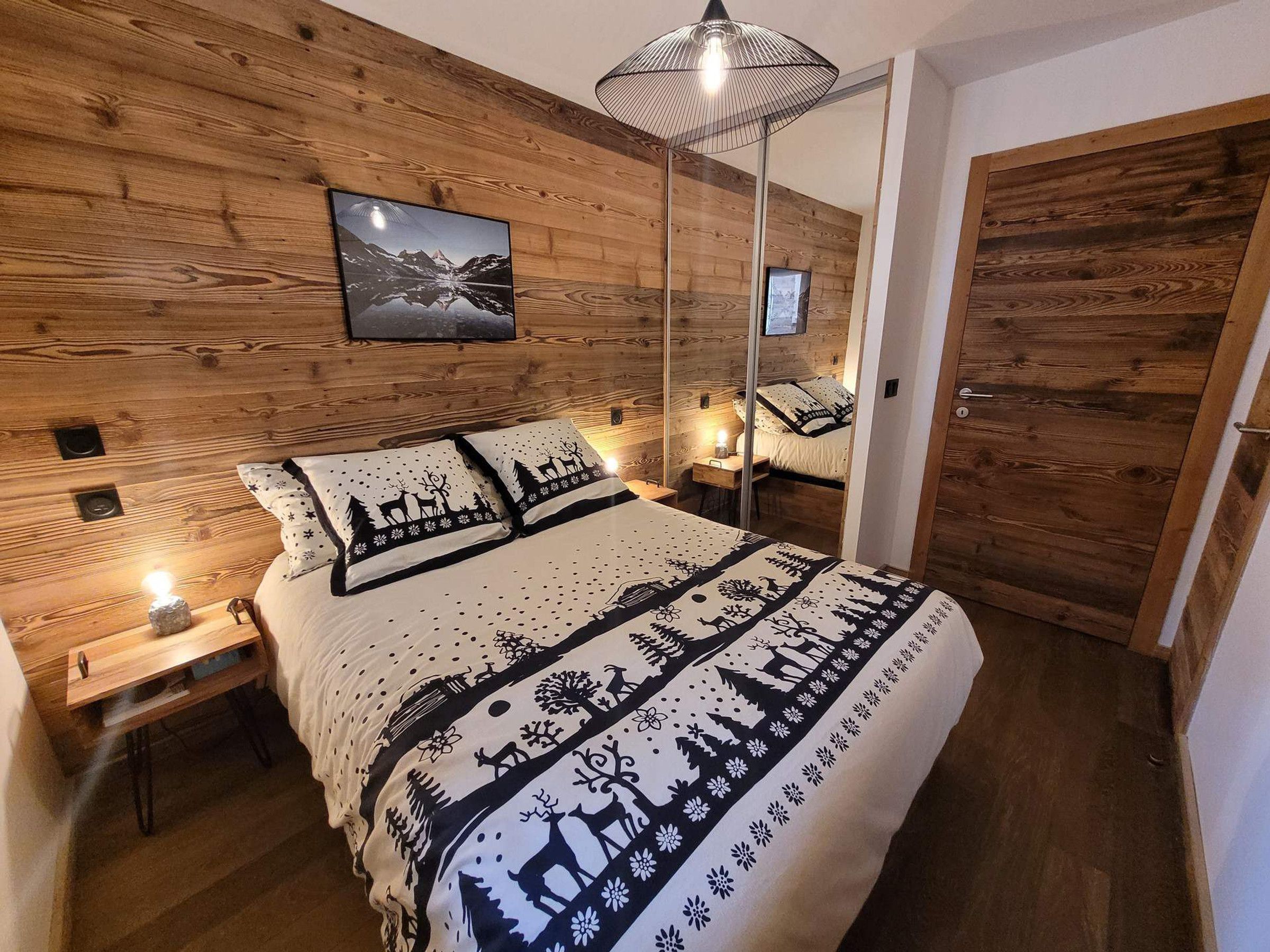 A cozy bedroom with a wooden headboard, a bed with patterned bedding, bedside lamps, and a mounted picture.