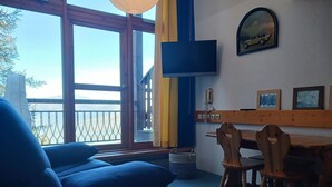 Ein Zimmer mit großem Fenster und Blick auf eine schöne Aussicht, einem Wand-Fernsehgerät und einem Holztisch mit Stühlen.