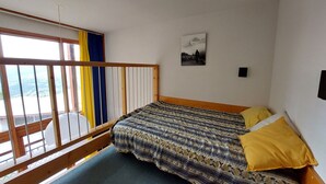Ein Schlafzimmer mit Bett, einem Vorhangfenster, einem Bild an der Wand und einem Balkon mit Geländer.