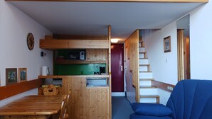 Ein gemütliches Zimmer mit einem Holzesstisch, einem blauen Sofa, einer Treppe und einer Küchenzeile mit Holzschränken und einer grünen Arbeitsplatte.