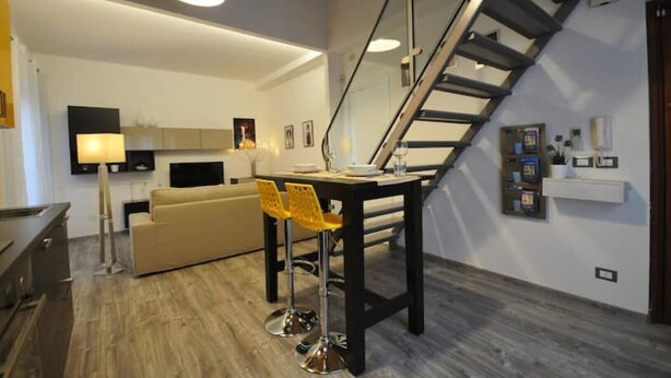 A modern living room with a staircase, a dining area with yellow chairs, and a sofa. - Papireto 11 Loft |Charming cozy space at Cathedral (Palermo)