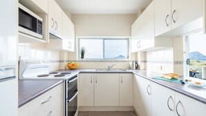 Een moderne keuken met witte kastjes, een fornuis, een magnetron en een raam met uitzicht op bergen.