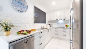 Une cuisine moderne avec des meubles blancs, un lave-vaisselle encastré, une grande fenêtre et une horloge décorative.