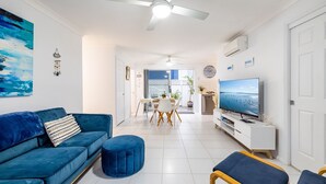 Un salon moderne avec un canapé bleu, un téléviseur et un coin repas comprenant une table et des chaises.