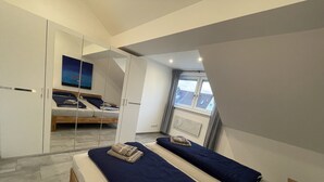 A bedroom with two beds, a wardrobe, a window, and a painting on the wall.