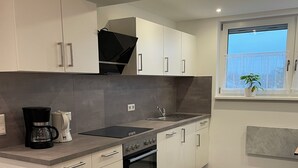 A modern kitchen with white cabinets, a built-in oven, a coffee maker, and a window with a plant.