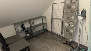 A small, well-organized room with a desk, ironing board, and a vacuum cleaner.