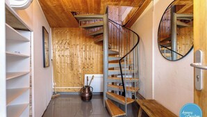 Una escalera de caracol con escalones de madera y barandillas de metal, una pared de madera con listones verticales, un espejo redondo en la pared y una puerta de metal con manija.