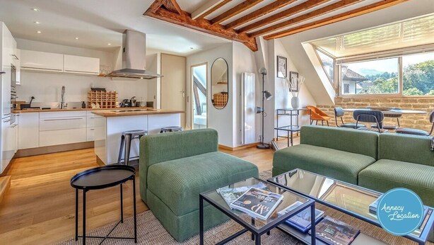 Una cocina moderna con armarios blancos y vigas de madera, un juego de sofá verde y una zona de comedor con mesa y sillas.