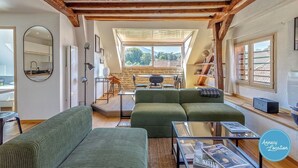 Un salón acogedor con sofás verdes, una mesita de centro de vidrio y vistas al exterior por un tragaluz.