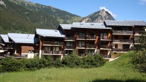 A row of wooden multi-story buildings with balconies, set against a mountainous backdrop.