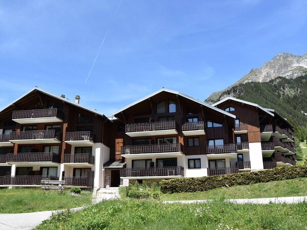 A multi-story wooden chalet with balconies, set against a mountainous backdrop.