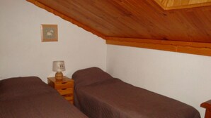 A small, single-room accommodation with two beds, a wooden nightstand with a lamp, and a framed picture on the wall.