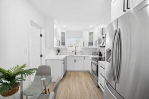 Une cuisine moderne avec des meubles blancs, un réfrigérateur en acier inoxydable et un coin repas comprenant une table et des chaises en verre.