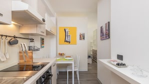A modern kitchen with white cabinetry, a central island, and a dining area with a white table and chairs. - BnButler - Archimede 53 (Milan)