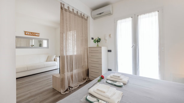 A modern hotel room with a bed, a sofa, a 'Welcome' sign, a mirror, and a window with curtains. - BnButler - Archimede 53 (Milan)