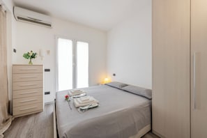 A hotel room with a bed, a bedside table with a lamp, a wardrobe, and a view of the outside through a window.