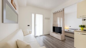 A modern living room with a sofa, TV, and a small kitchen area with a sink and countertop. - BnButler - Archimede 53 (Milan)