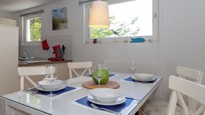 A dining area with a table set for two, a window with a view of greenery, and a hanging lamp. - 3-zi-fewo für Max. 4 Pers. im DG, Wlan, Strandnah (Graal-Müritz)