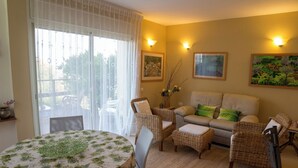 A living room with a round table, wicker chairs, a sofa, and two wall-mounted lights. - Bait Bagiva (Gan Rave)