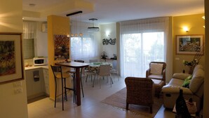 A spacious living area with a dining table, chairs, a sofa, and a kitchen area with a microwave. - Bait Bagiva (Gan Rave)