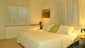 A bedroom with a bed, a bedside table, a lamp, and a painting on the wall. - Bait Bagiva (Gan Rave)
