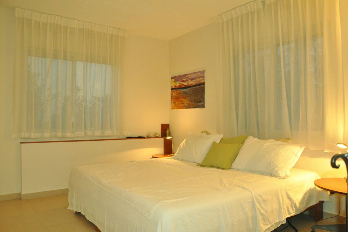 A bedroom with a bed, a bedside table, a lamp, and a painting on the wall.
