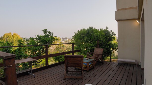 A wooden deck with outdoor furniture, including chairs and a table, overlooking a garden area. - Bait Bagiva (Gan Rave)