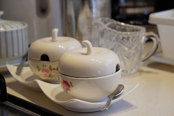 Two white teapots with floral designs on a white tray with a spoon, a clear glass pitcher, and a white container in the background.