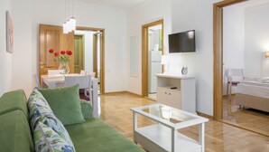 A modern living room with a green sofa, a glass coffee table, and a dining area with a white table and chairs. - Apartments IvanBeg (Belgrade)