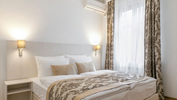 A neatly made bed with a patterned bedspread, two bedside tables with lamps, and sheer curtains. - Apartments IvanBeg (Belgrade)