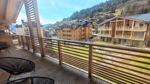 Une terrasse en bois avec deux chaises noires, d’où l’on peut admirer un village aux maisons traditionnelles en bois, avec des montagnes en toile de fond.