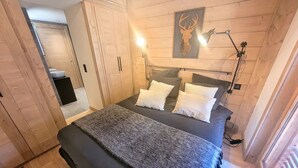Une chambre à coucher comprenant un lit, des oreillers, une tête de lit, une lampe fixée au mur et une tête de lit en bois ornée d’une tête de cerf.
