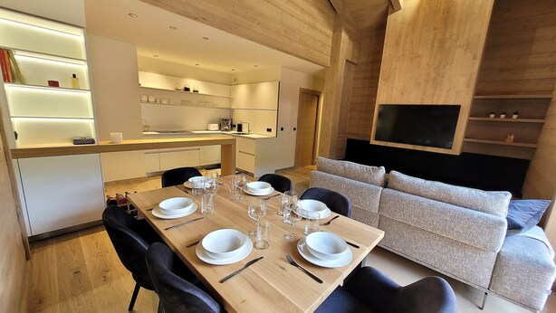 Un espace de repas moderne avec une table en bois dressée pour six personnes, des chaises noires et un canapé en arrière-plan.