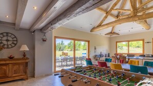 A spacious room with a foosball table, large windows, and a rustic ceiling.