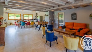 A spacious room with a wooden ceiling, a dining area with colorful chairs, a sofa, and a foosball table.