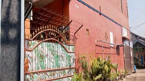 Un edificio rojo con una verja metálica decorativa y macetas con plantas en la entrada.
