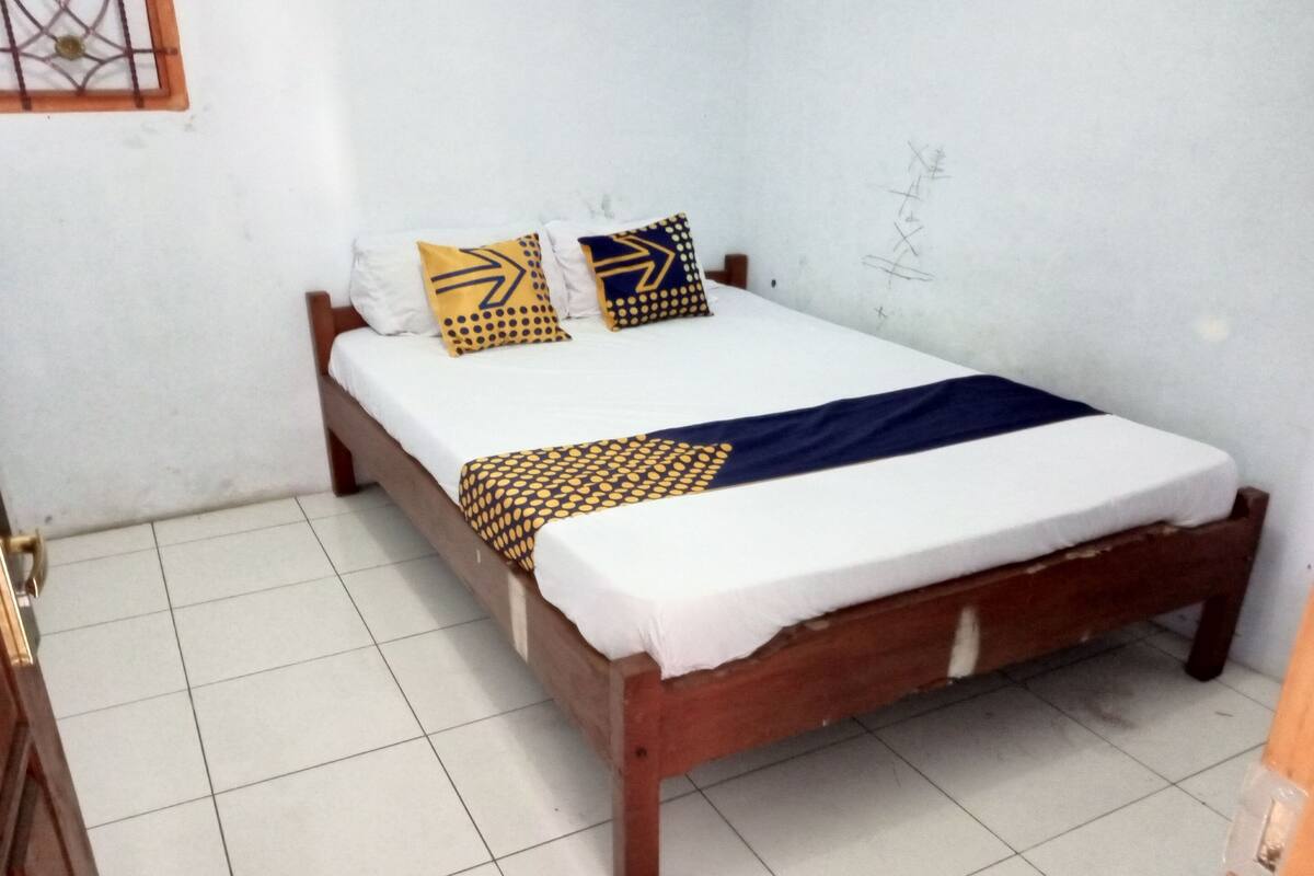 Een eenpersoonsbed met houten frame, wit beddengoed en gestreepte kussens.