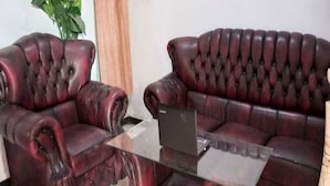 Una habitación con dos sofás de cuero rojo oscuro y una mesa de centro de vidrio con un ordenador portátil.