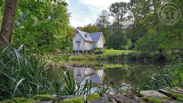 Ein Haus am Ufer eines stillen Teichs, im Vordergrund eine Holzterrasse.