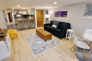 A modern living room with a sofa, ottoman, and a dining area with chairs.