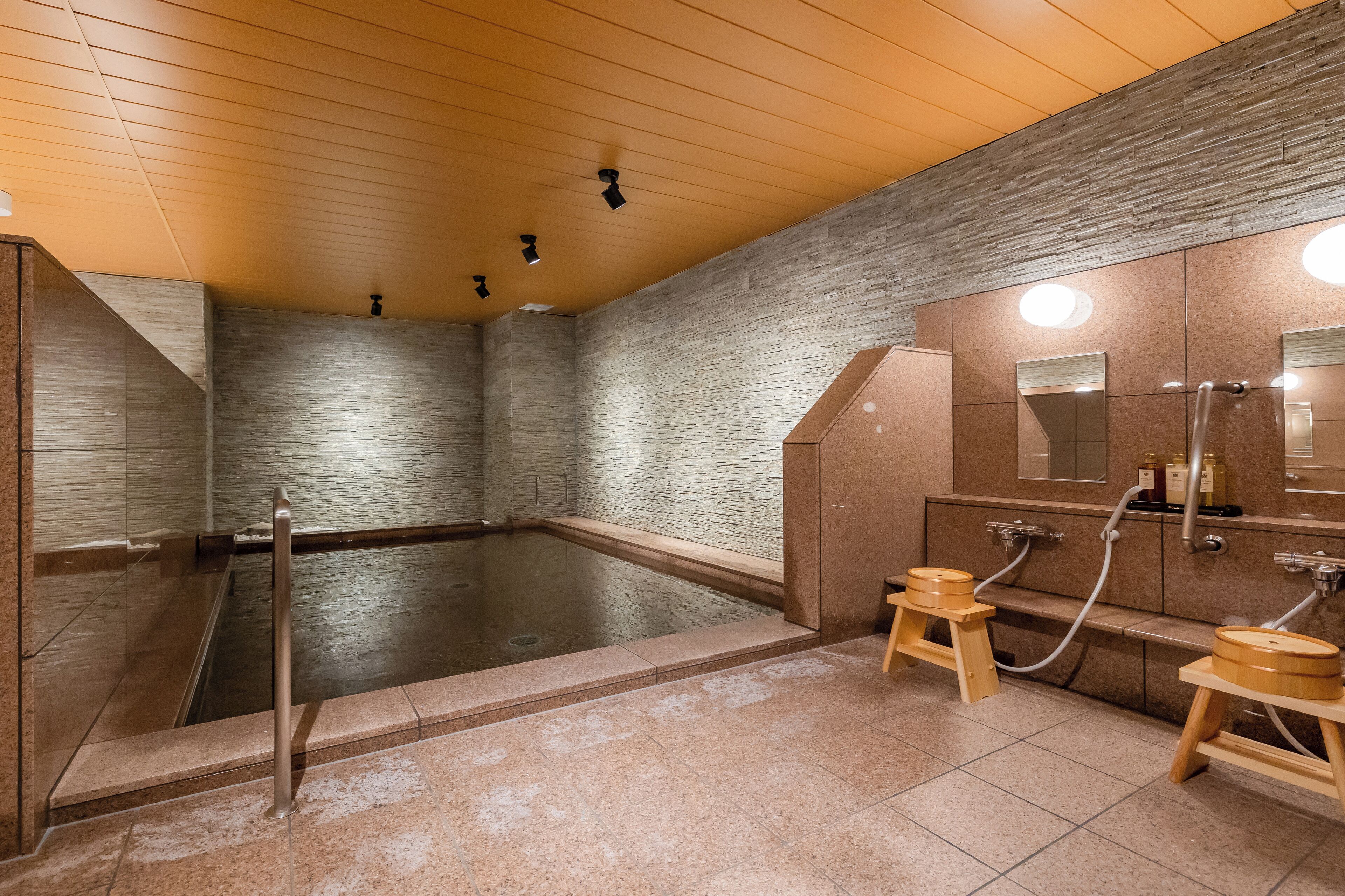 A modern spa with a large hot tub, wooden stools, and a wooden ceiling.