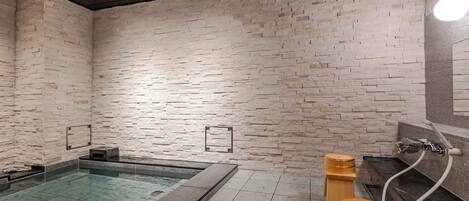 A modern spa area with a stone wall, a glass-enclosed hot tub, and wooden barrels.