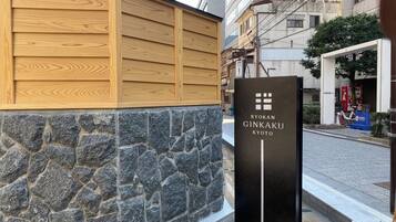 A Ryokan Ginkaku Kyoto sign with a stone wall and wooden panel facade.